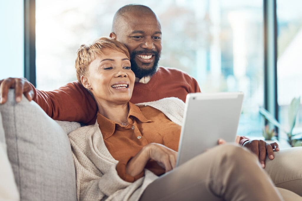Senior black couple, tablet on sofa or reading social network, email or communication with smile. M